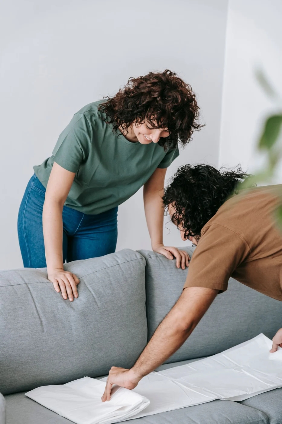 Two people protecting a sofa with a cloth cover